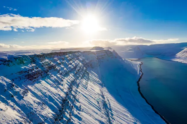 Aerial of snow-covered mountains above a fjord in low winter sun, Iceland
