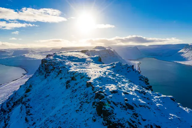 Aerial of a snow-covered mountain ridge between fjords in winter sun, Iceland