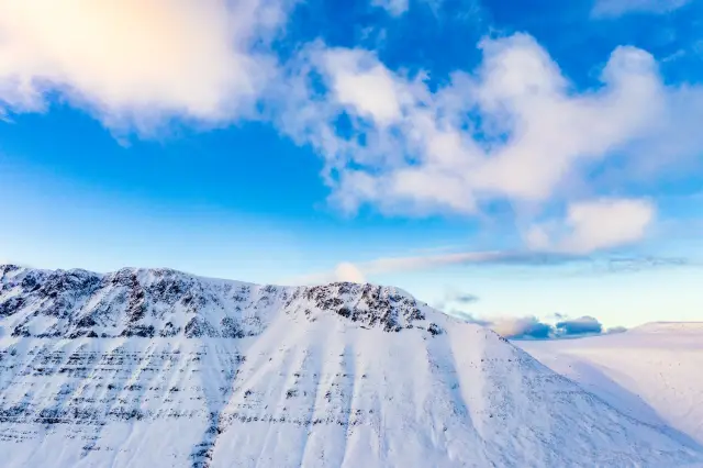 A snow-covered mountain ridge sweeping under a bright blue sky scattered with clouds.