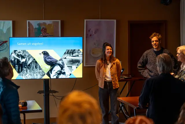 A speaker presenting to an audience beside a screen.